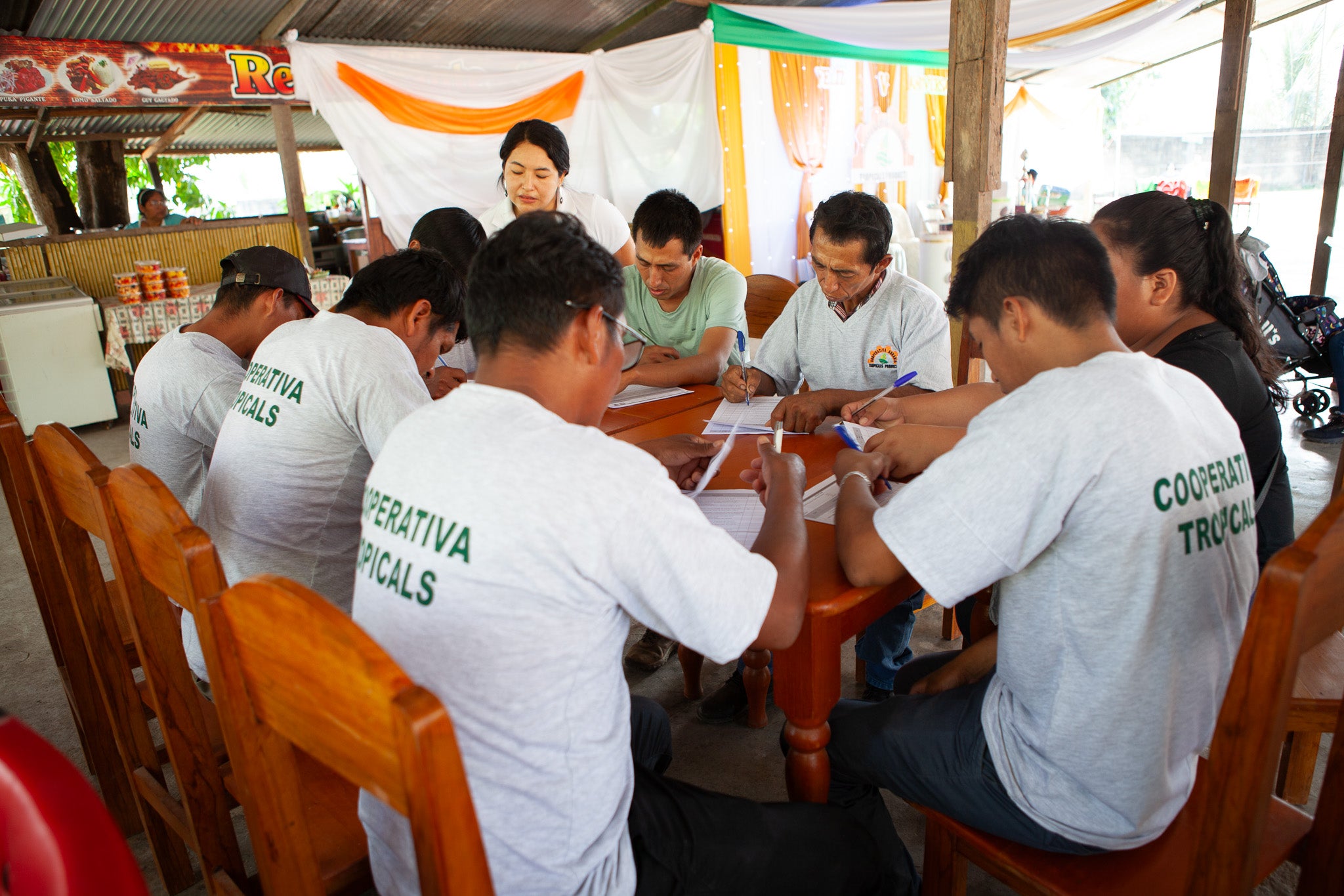 Group of people in white shirts with 'Cooperativa Tropicals' printed on them, sitting around a table.